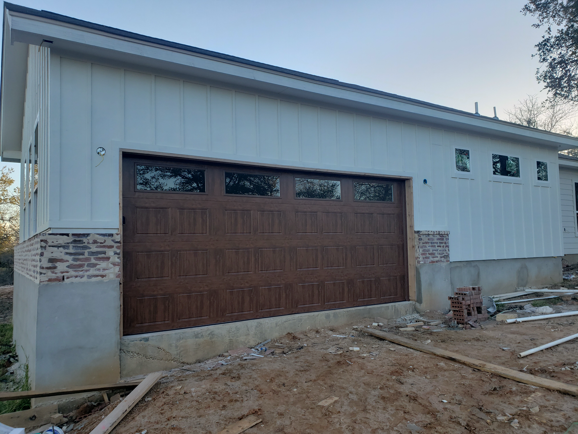 A white house with a brown garage door is being built.