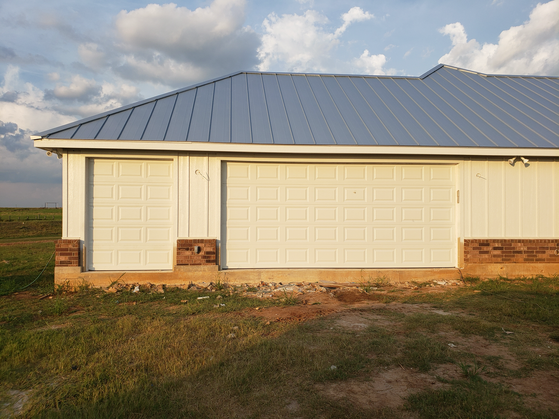 A white garage with a metal roof is in the middle of a grassy field