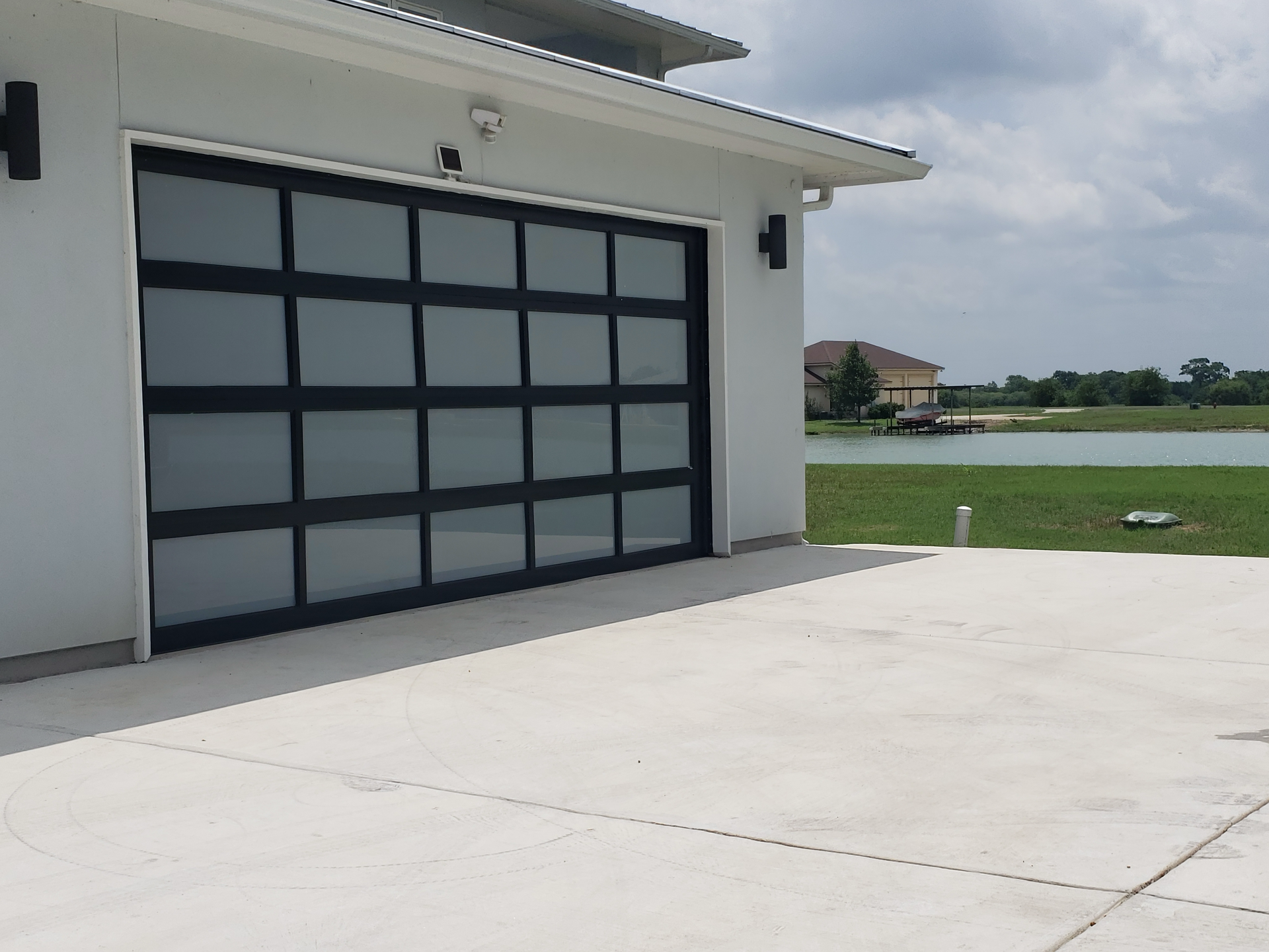 A white house with a black garage door is next to a lake.