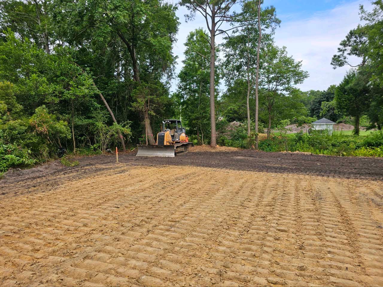 A bulldozer is moving dirt in a field with trees in the background.