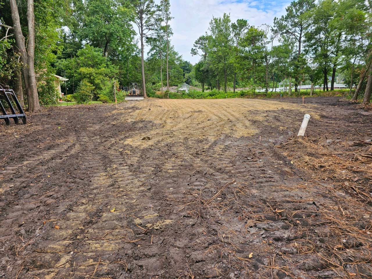 A muddy field with trees in the background and a tractor in the foreground.
