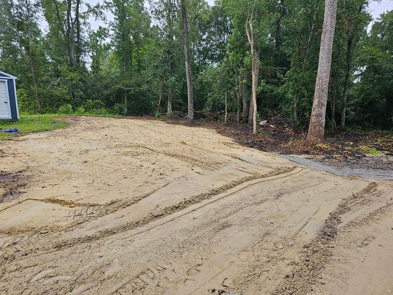 A dirt road with trees in the background and a shed in the background.