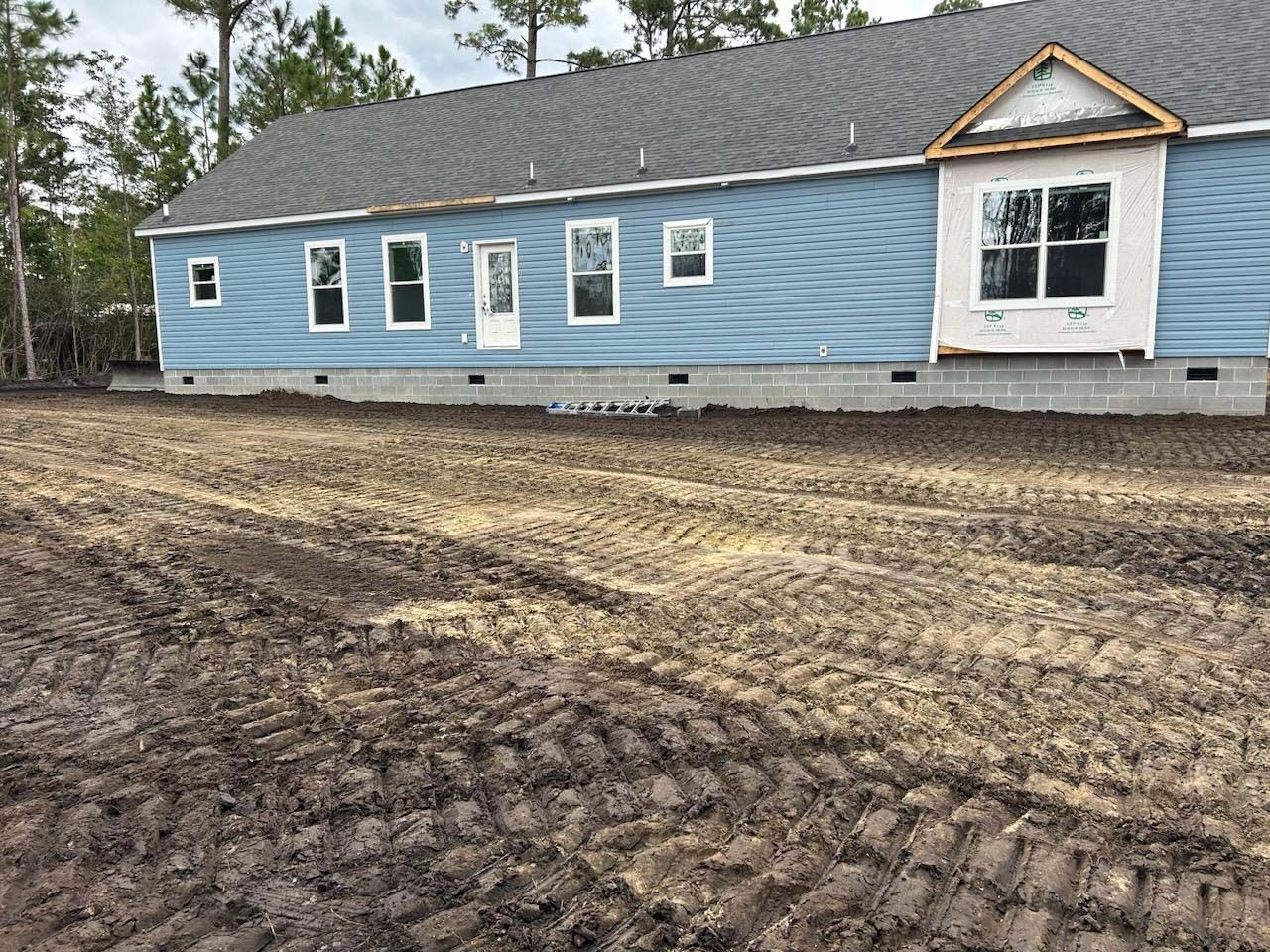 A blue house is sitting in the middle of a dirt field.