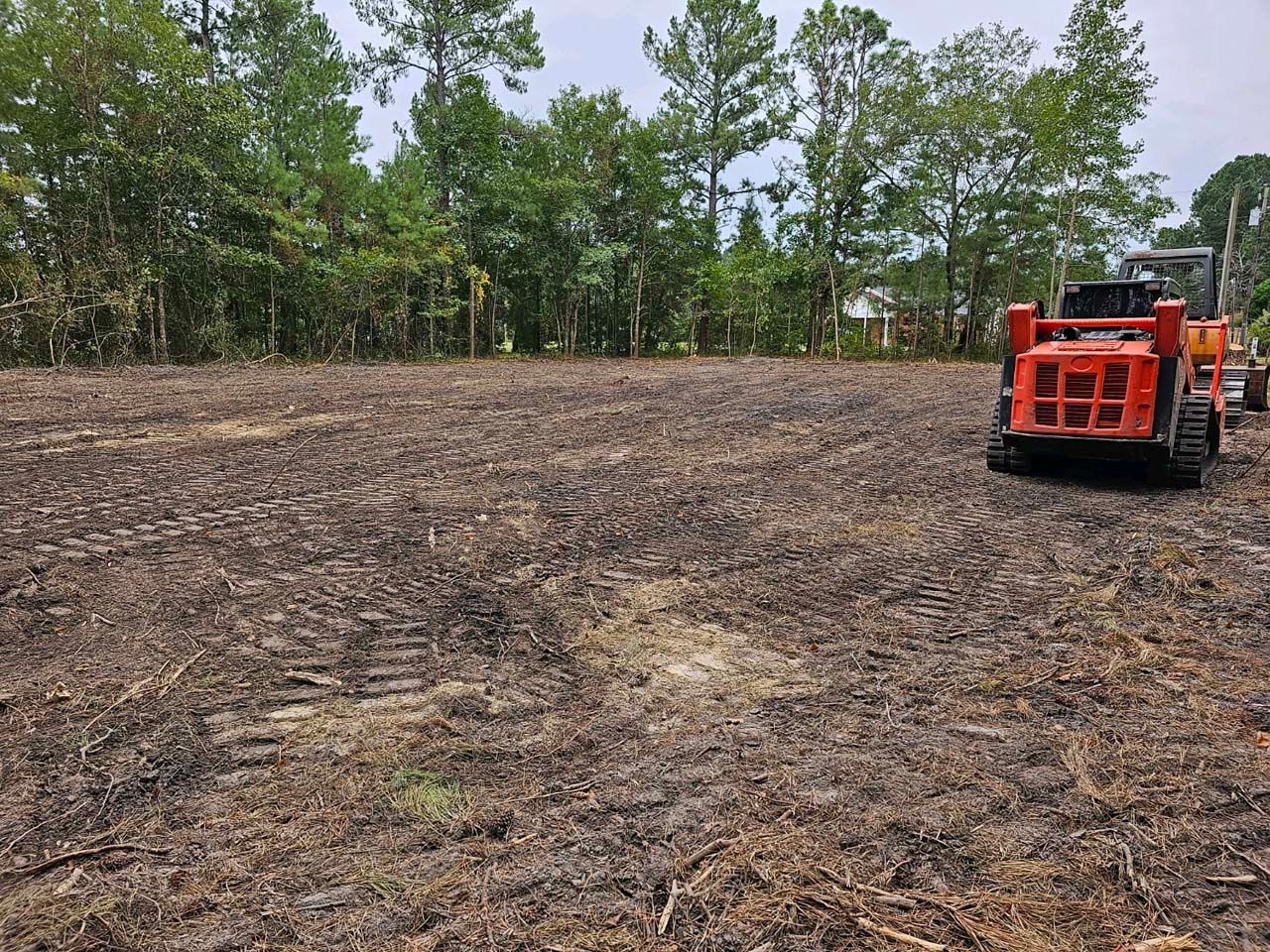 A tractor is driving through a dirt field with trees in the background.