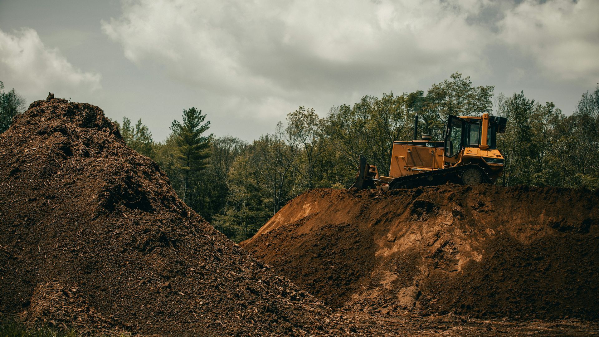 A yellow bulldozer is sitting on top of a dirt hill.
