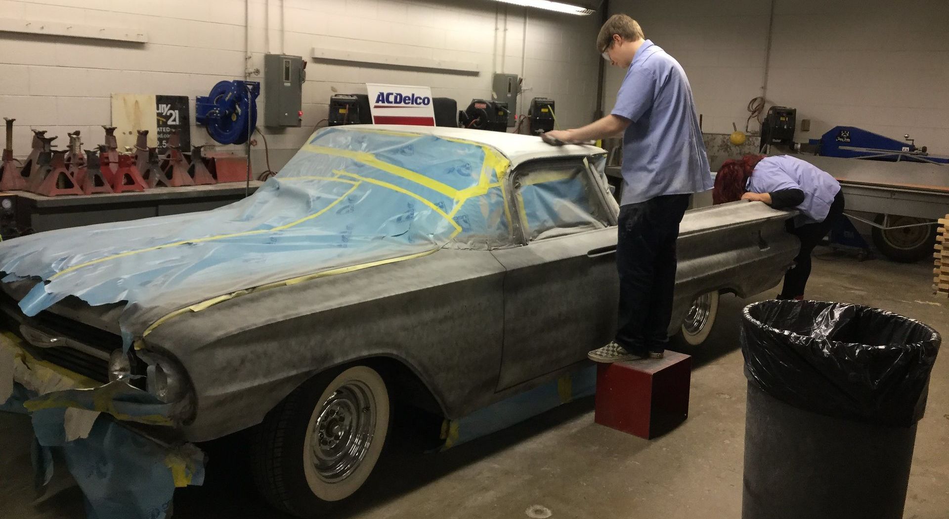 A man in a blue shirt is painting a car in a garage