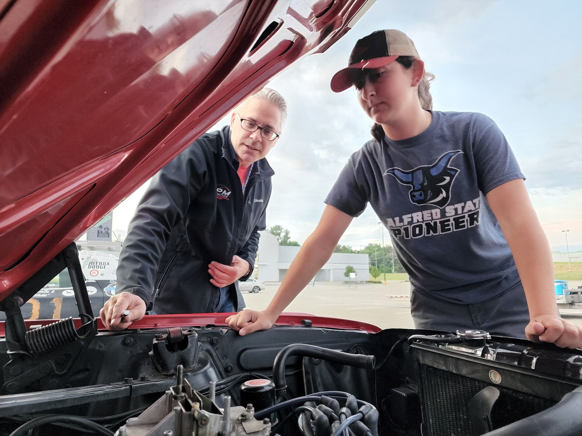 A man and a woman are looking under the hood of a car.