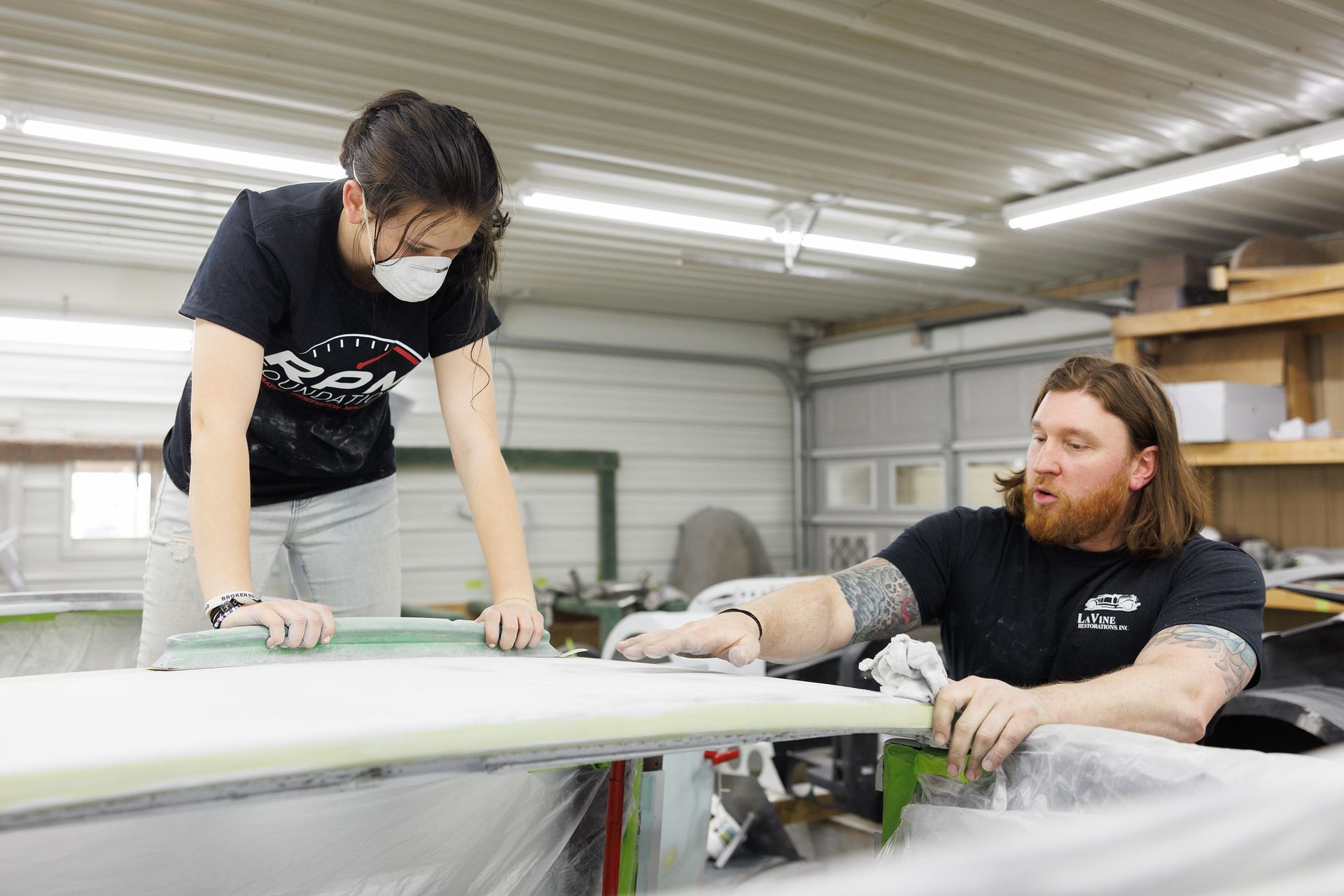 A man and a woman are working on a surfboard in a garage.