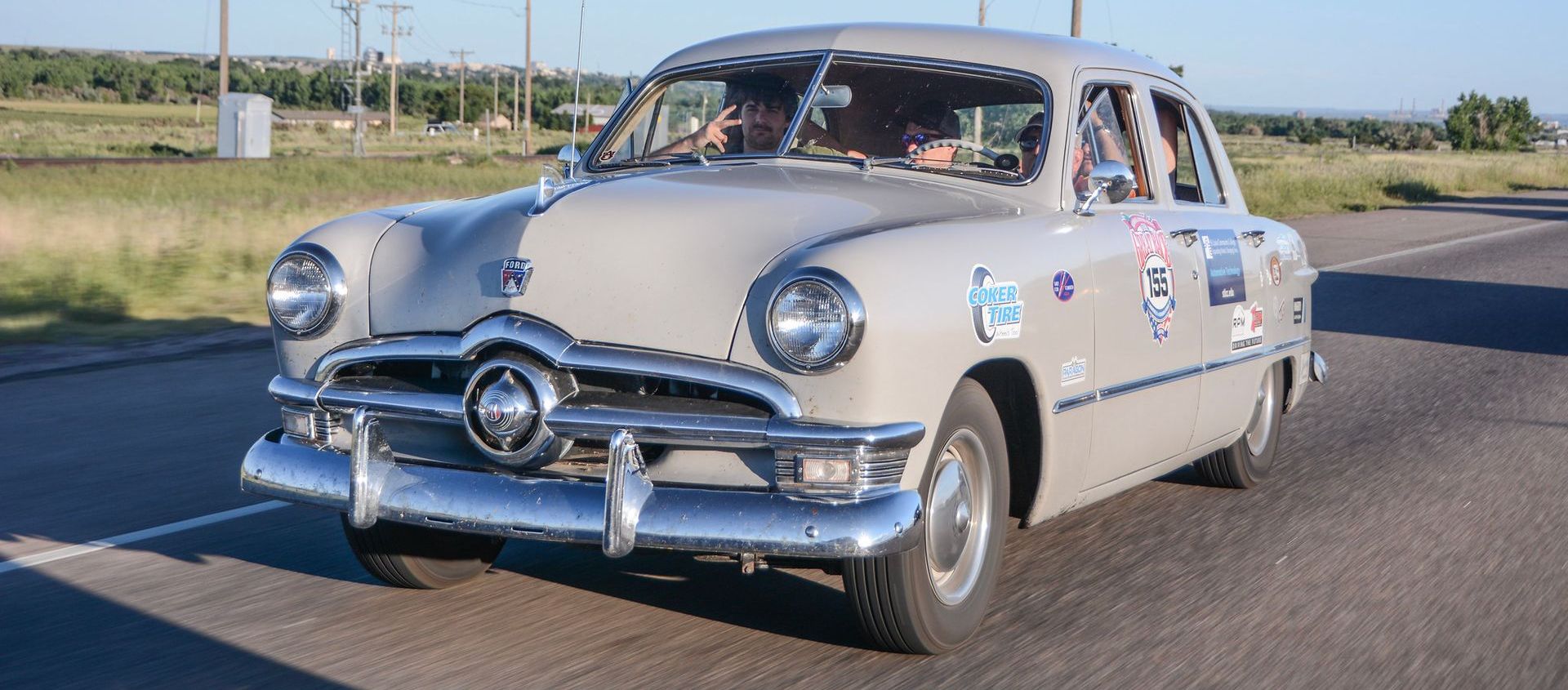 An old ford car is driving down the road