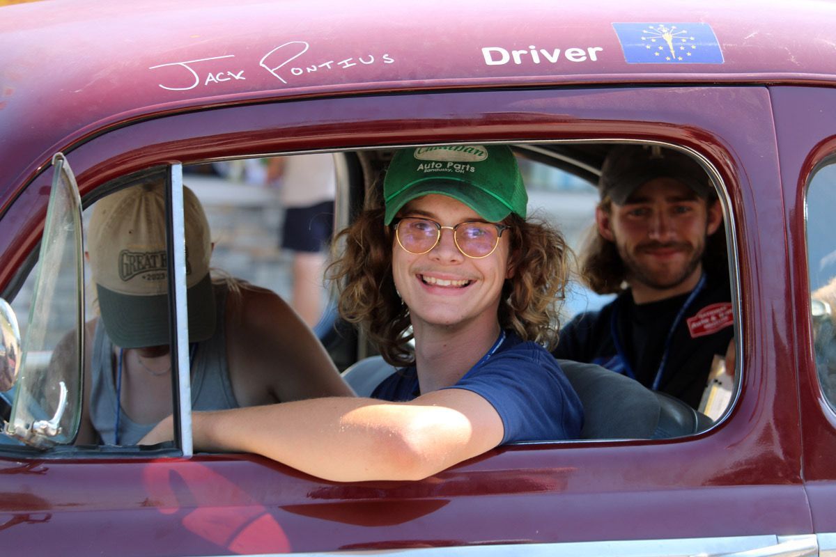 A man in a green hat is smiling while sitting in a car.