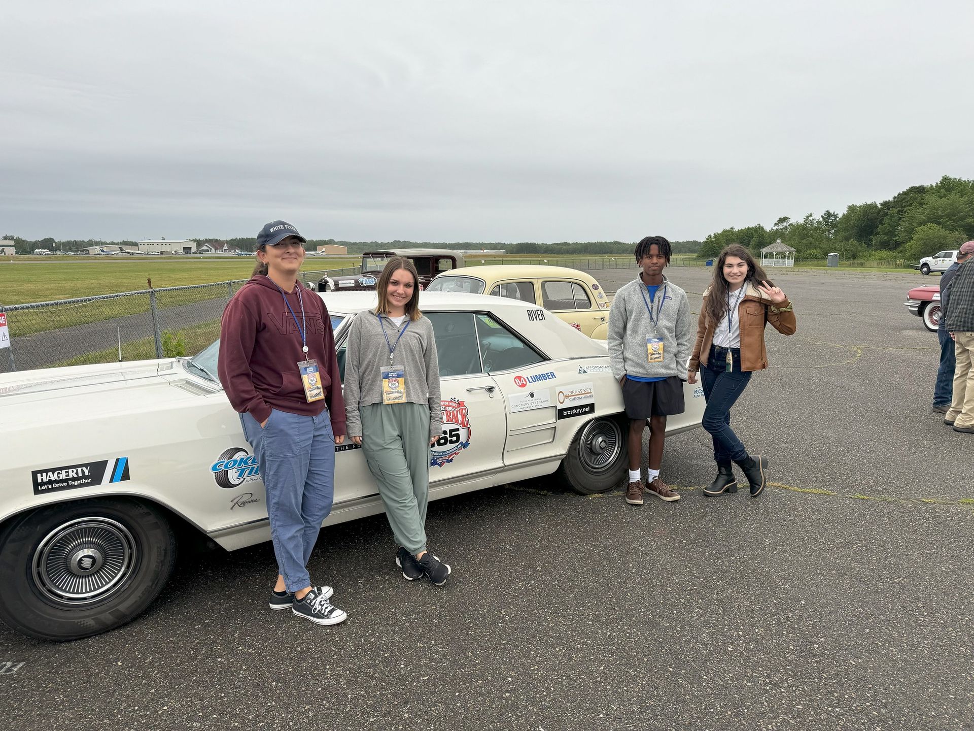 A group of people are standing next to a white car in a parking lot.