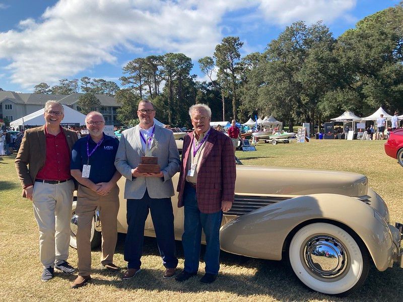 A group of men standing in front of an old car