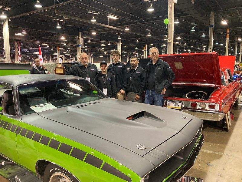 A group of men are posing for a picture in front of a green and gray car.