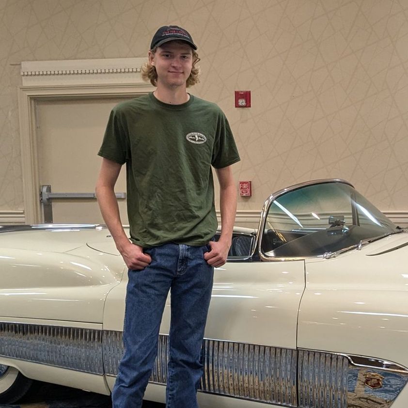 A young man in a green shirt is standing next to a white car