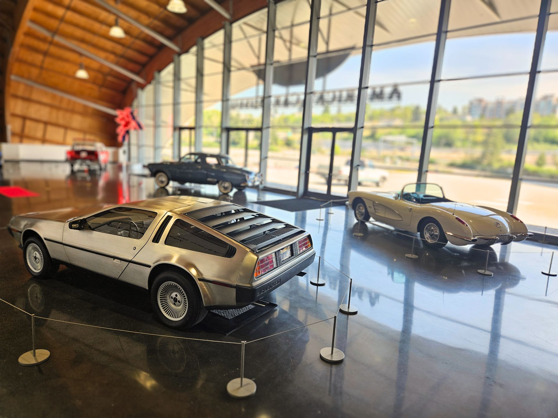 Two cars are on display in a building with a lot of windows.