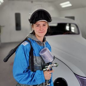 A young woman with a paint gun in an automotive paint booth.