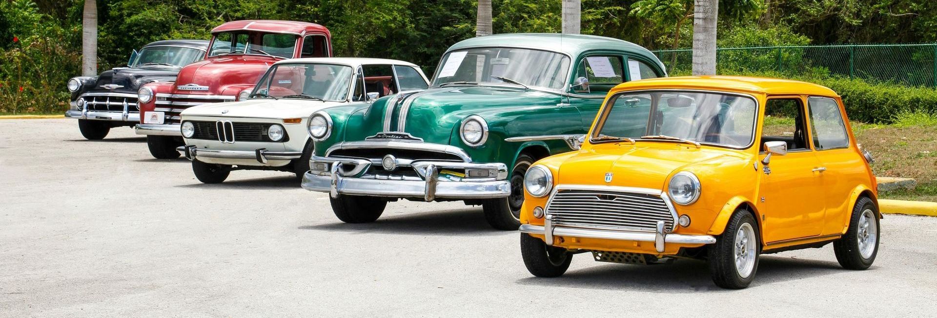 A row of old cars are parked in a parking lot