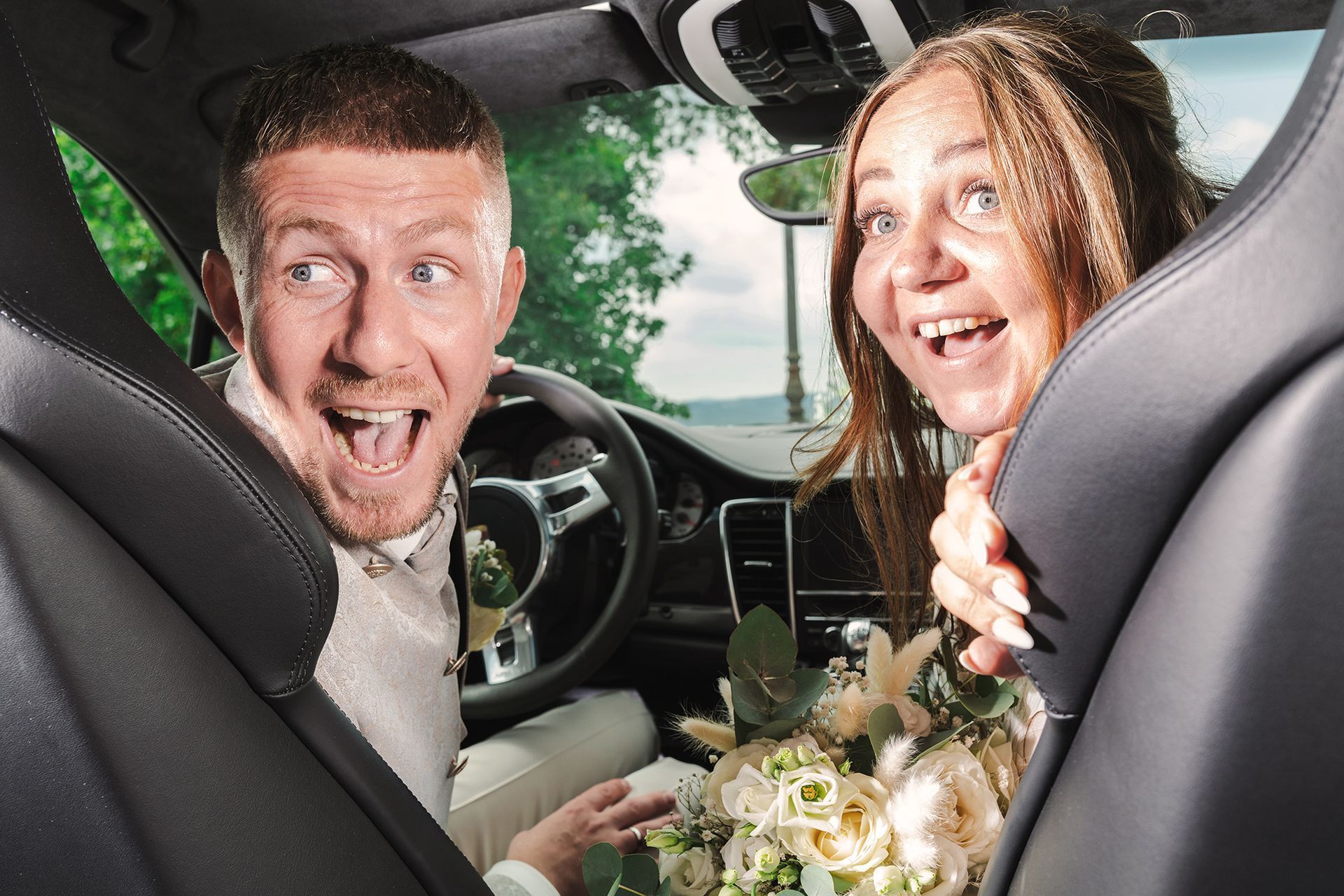 Lustige Hochzeitsfotografie im Auto. Das Brautpaar hat richtig viel Spaß bei der Abreise.