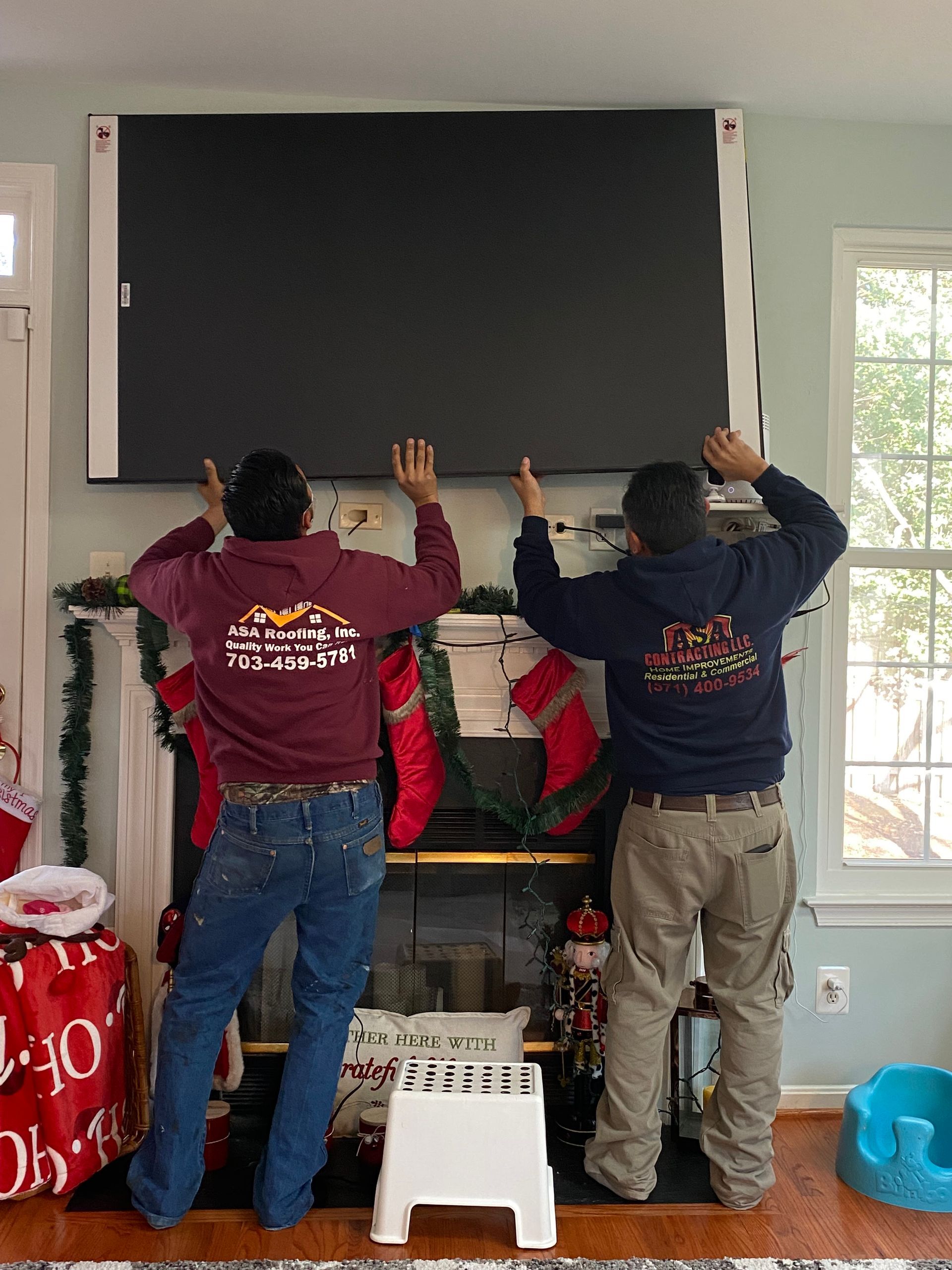 Two men are installing a flat screen tv on a fireplace.