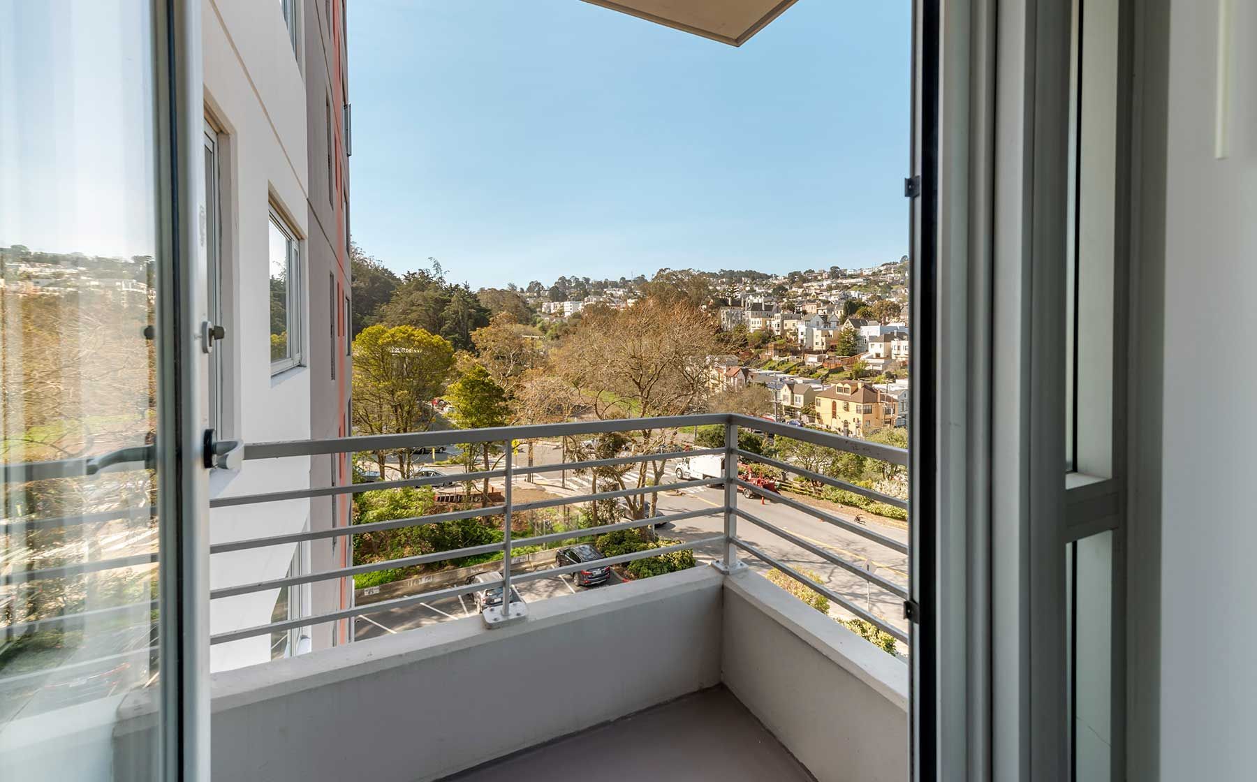 Balcony view of city, trees, and buildings on a sunny day.