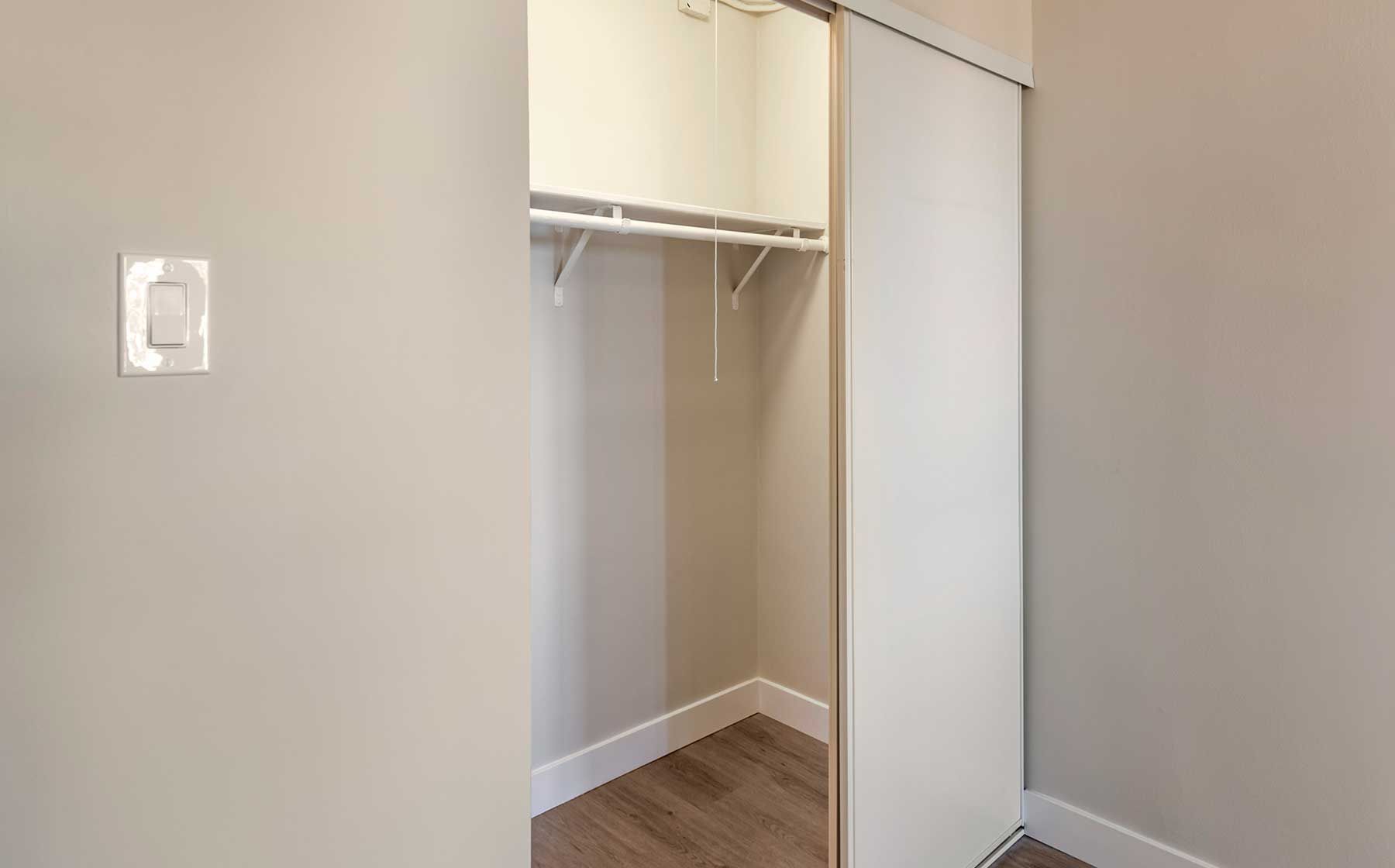 Empty closet with white sliding door, light wood floor, and beige walls.