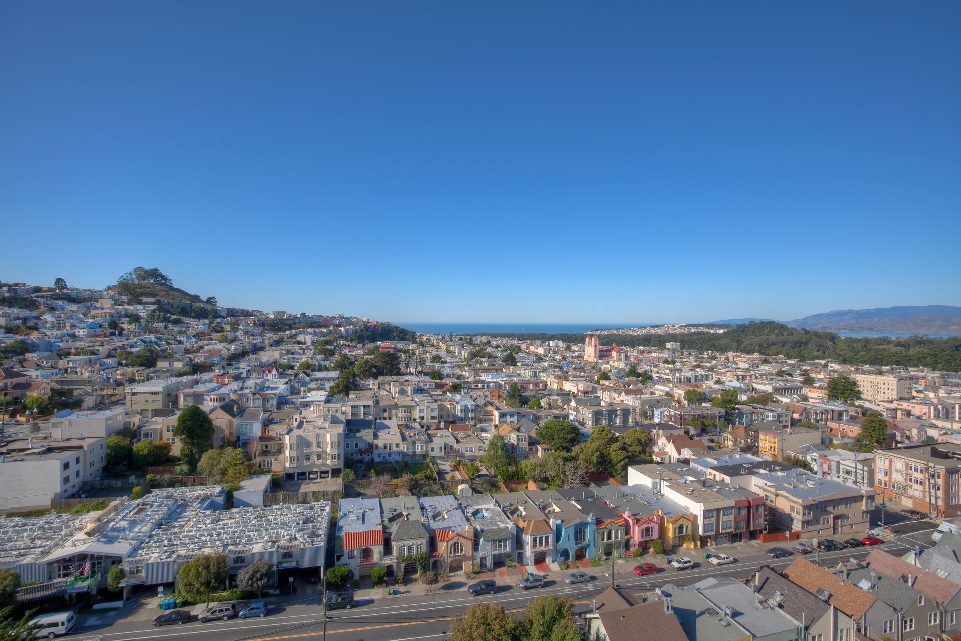 Cityscape view of colorful buildings under a clear blue sky, with a mountain in the background and ocean in the distance.