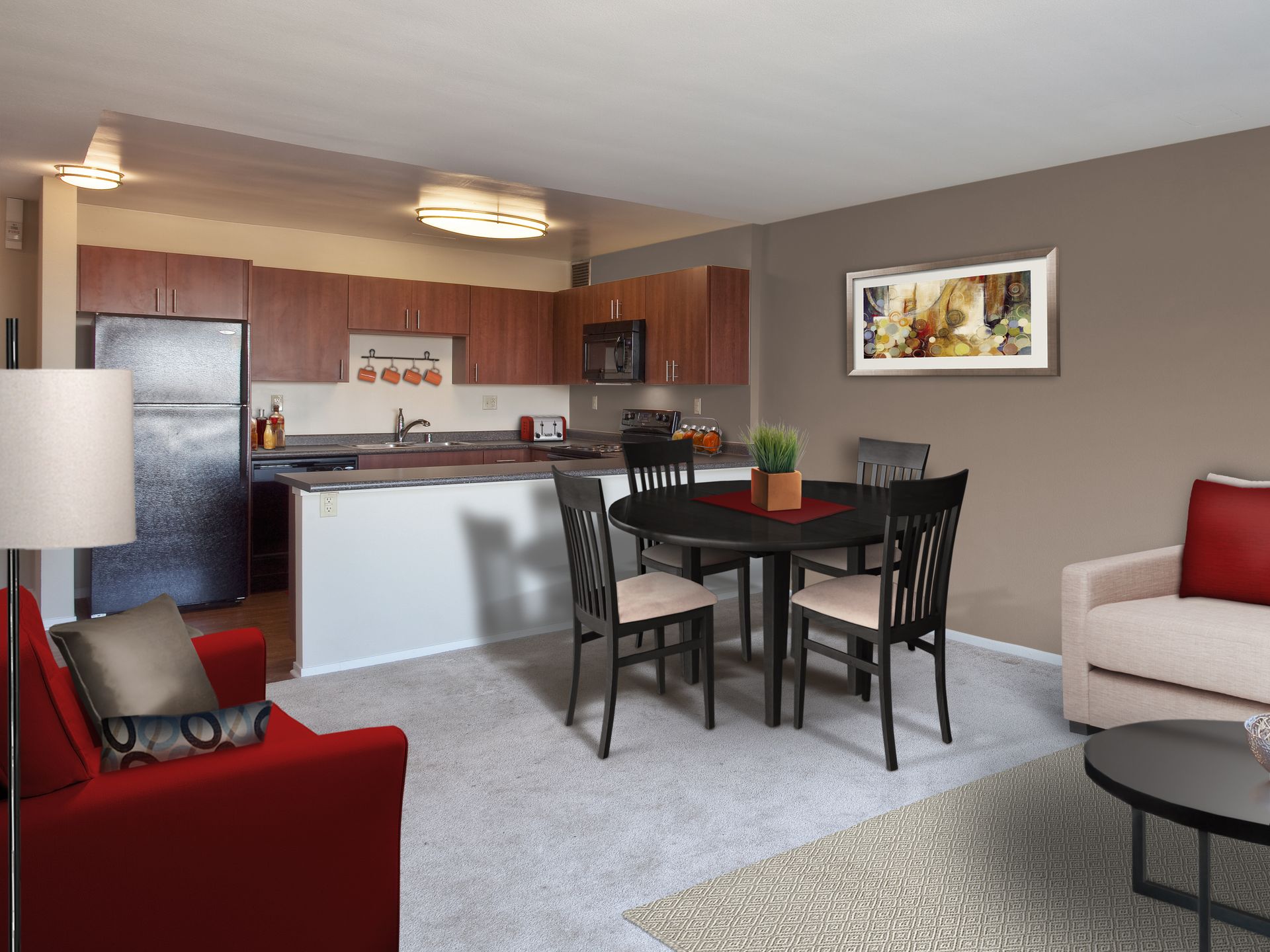 Open-concept living space with kitchen, dining area, and living room. Brown cabinets, dark appliances, gray carpet, red and beige furniture.