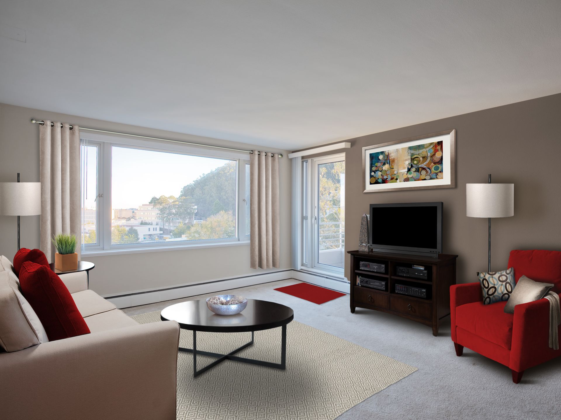 Living room with tan couch, red chair, TV, round coffee table, large window with view.