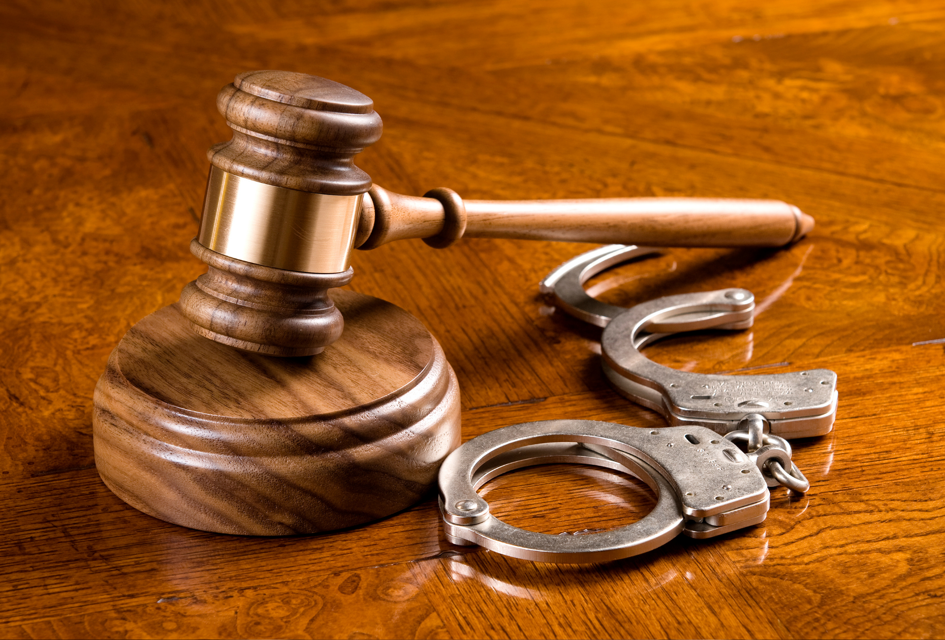 Wooden gavel and handcuffs on a wooden surface, suggesting legal proceedings.