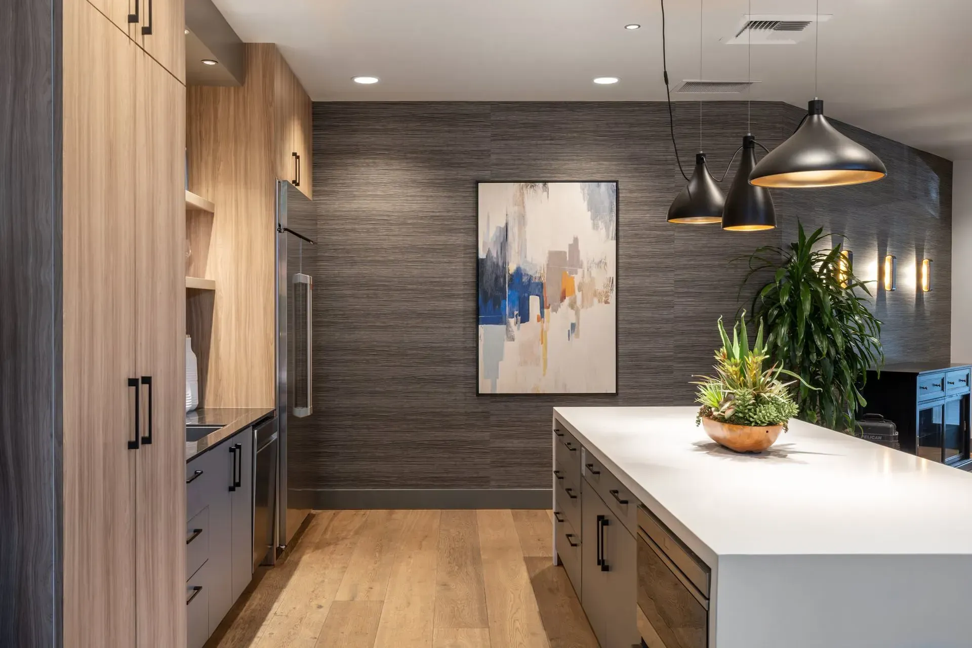 Modern kitchen featuring an oversized island, fridge, spacious cabinets, and designer lighting.