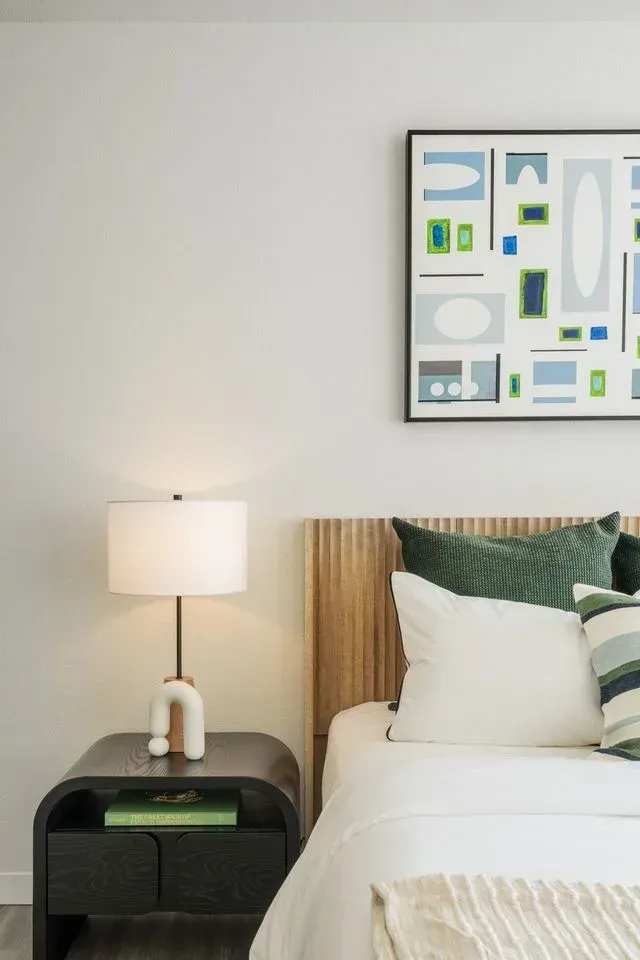 A bedroom with a bed , nightstand , lamp and painting on the wall