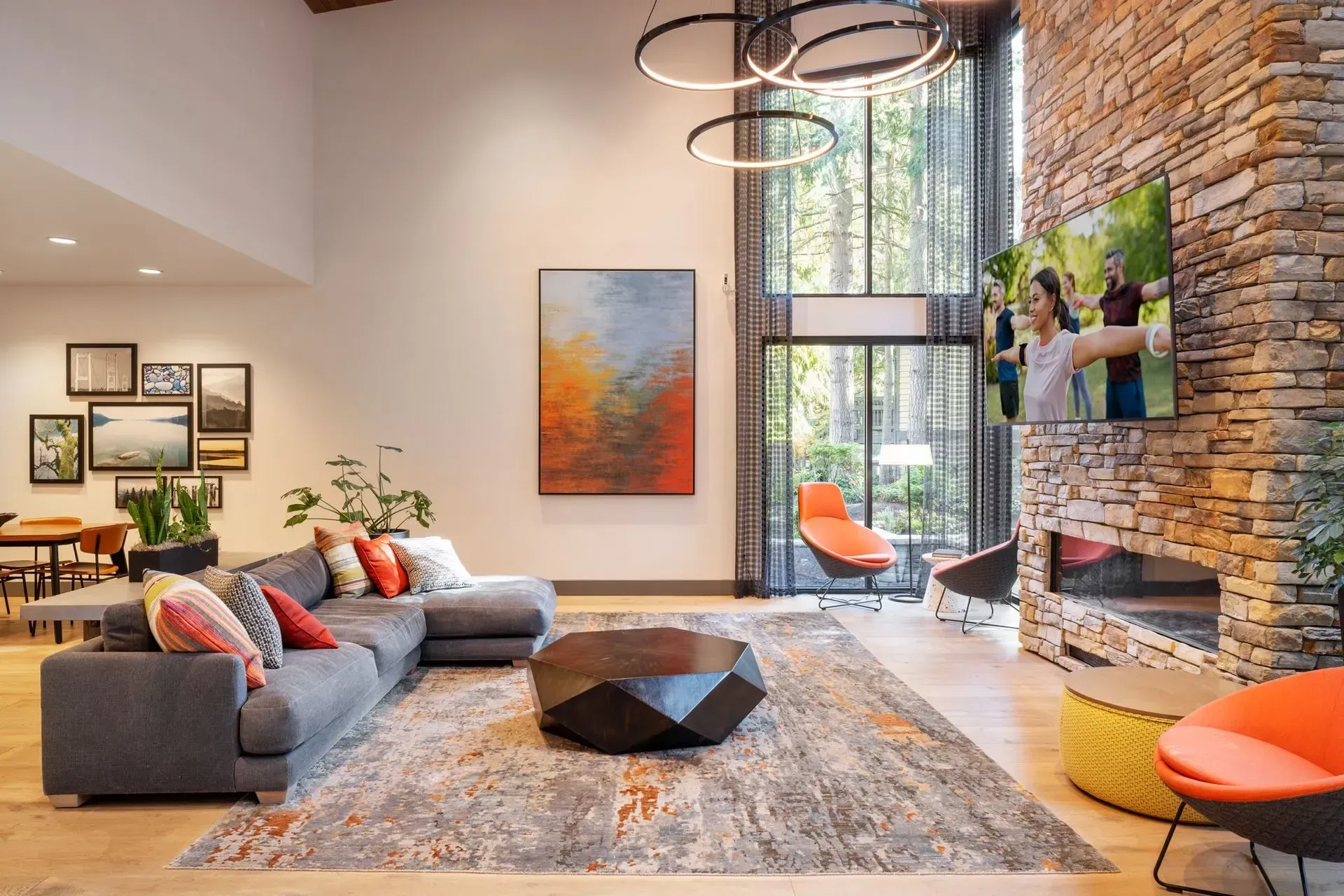 High-ceiling clubhouse featuring oversized windows, a sofa, coffee table, TV, and fireplace.