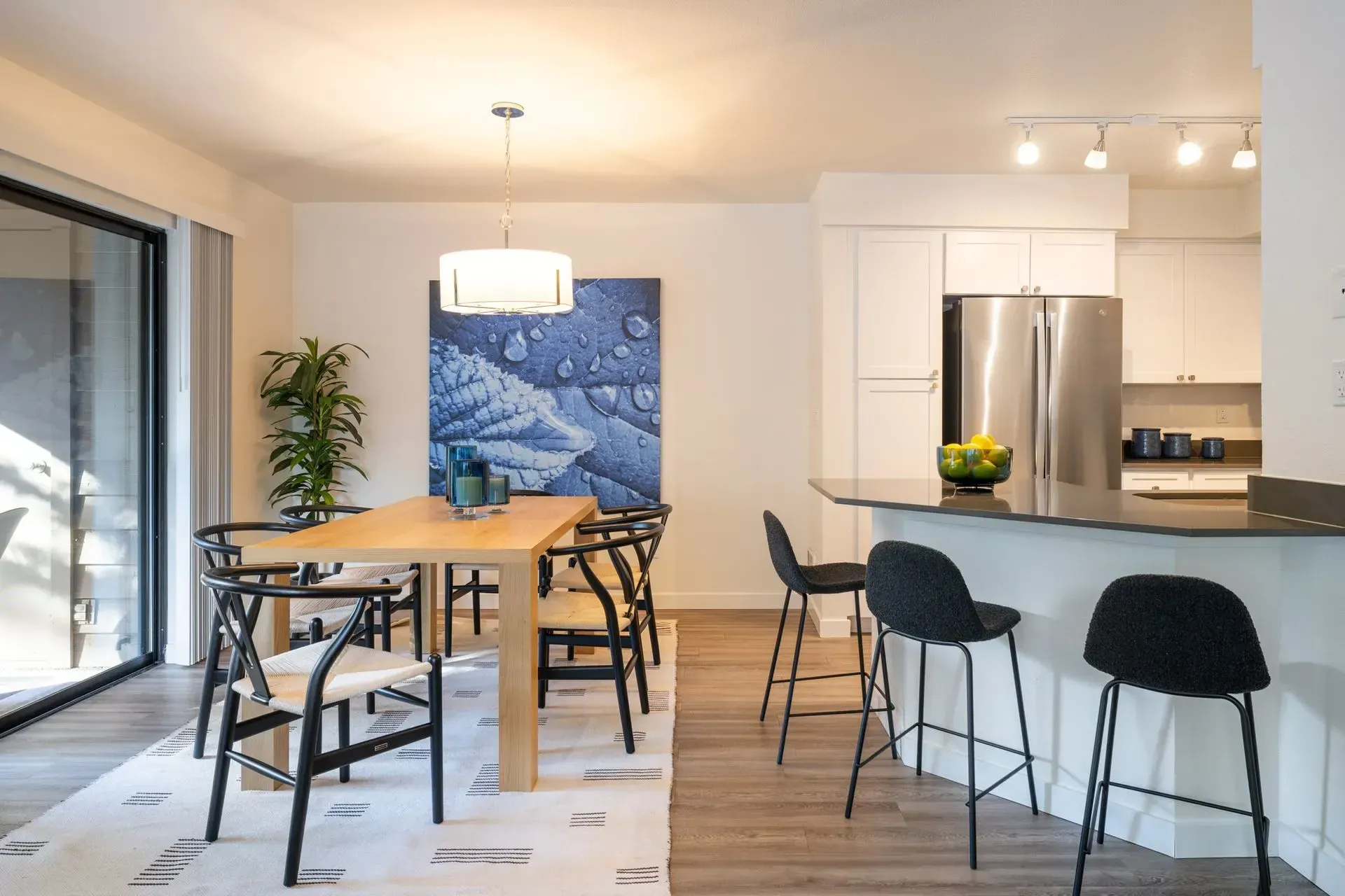 Apartment dining room and kitchen featuring a table, chairs, oversized window, kitchen island, bar chairs, and designer lighting.