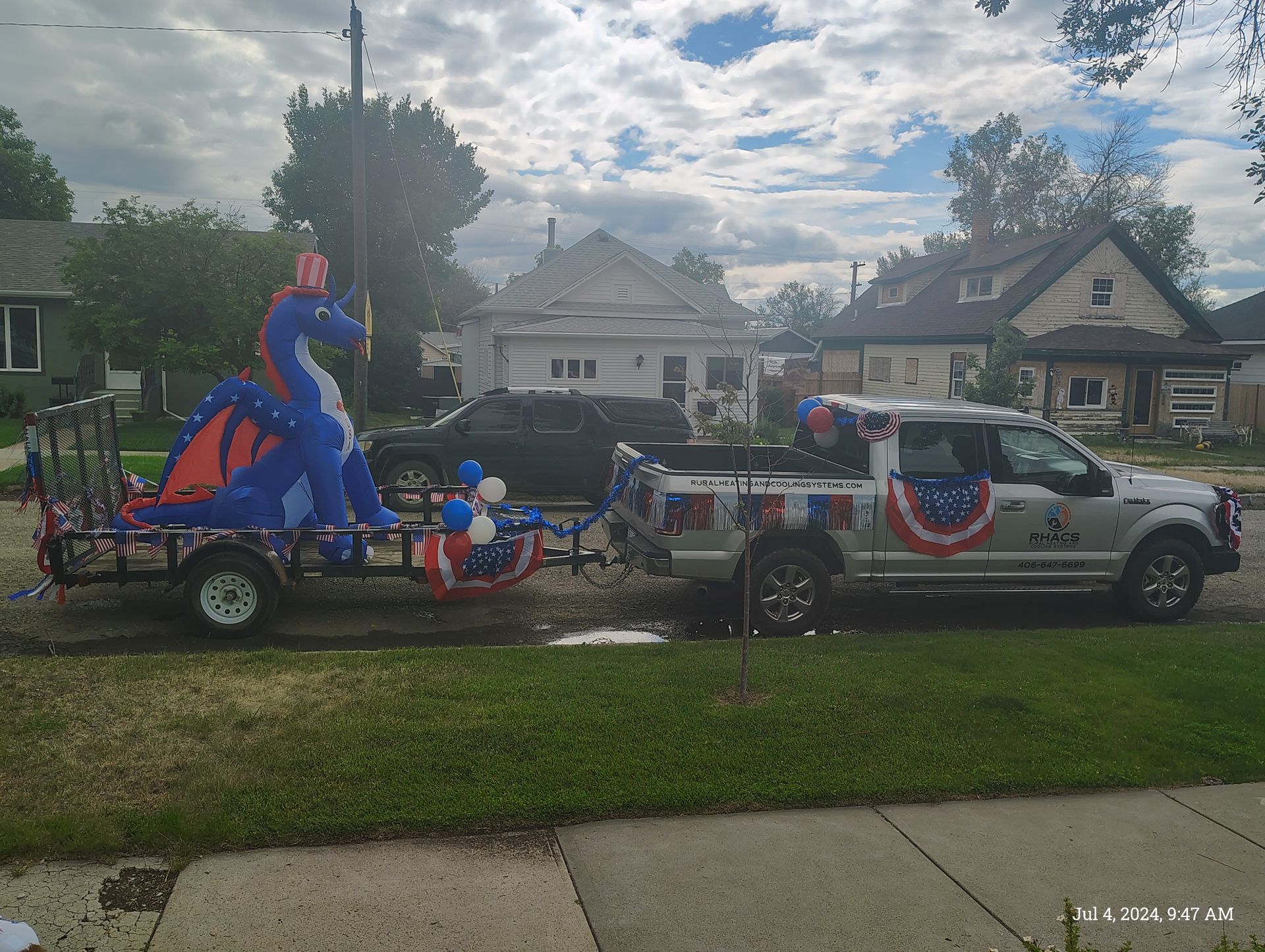 A line of parked vehicles, including police and work trucks, on a street in front of a two-story red house.