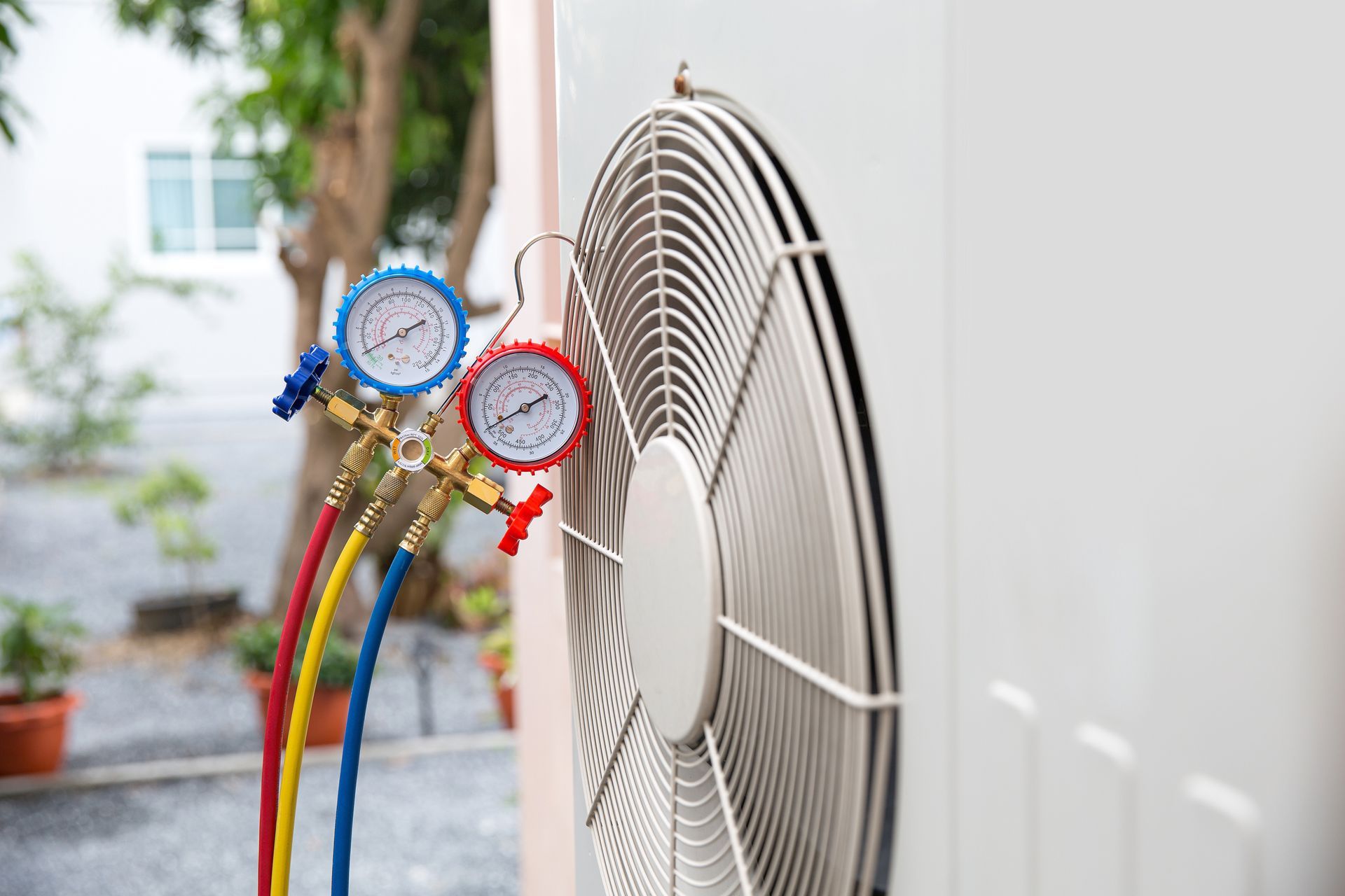 HVAC unit with gauges attached; outdoor setting. Red, blue, and yellow hoses connected to the unit.