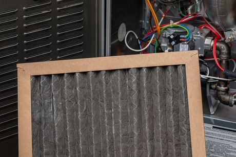 Dirty air filter being removed from a furnace, showing dust and debris accumulation.