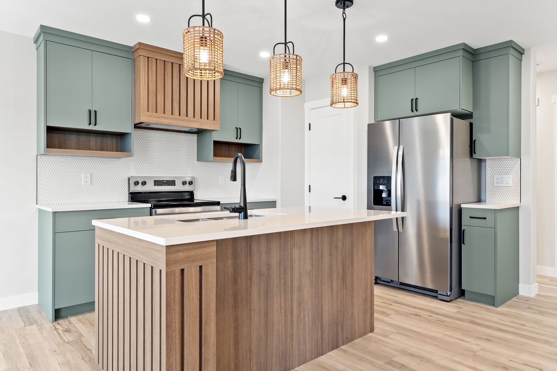 Modern kitchen with sage green cabinets, wooden island, stainless steel appliances, and pendant lights.