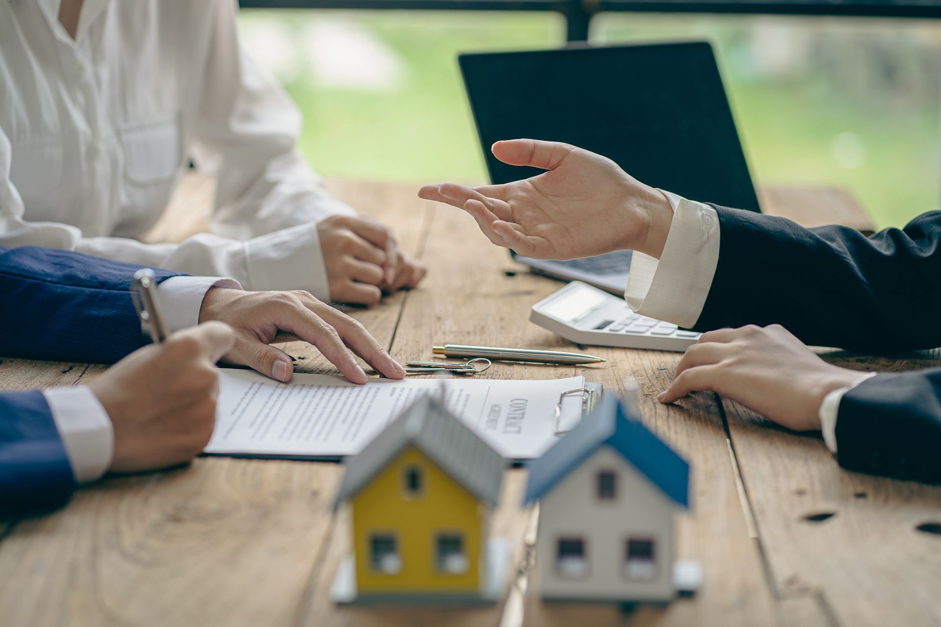 A Group of People Are Sitting at a Table With Miniature Houses and a Laptop