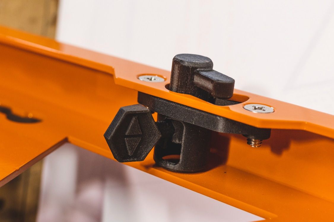 Clip et bouton imprimés en 3D noirs fixant une pièce noire à un cadre métallique orange à l'aide de vis.