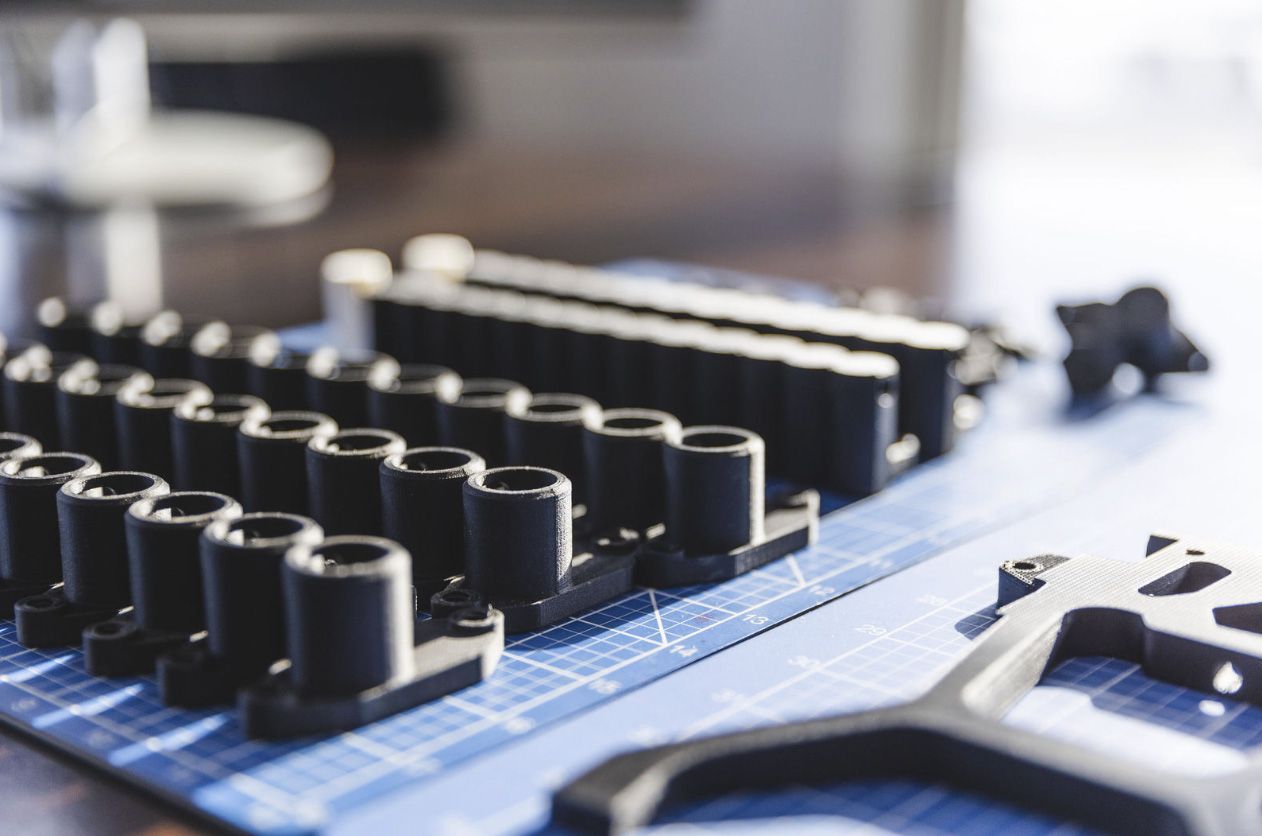 Des pièces en plastique noir disposées sur une grille bleue ; certaines sont cylindriques, d'autres ont des formes plus complexes, dans un contexte industriel.