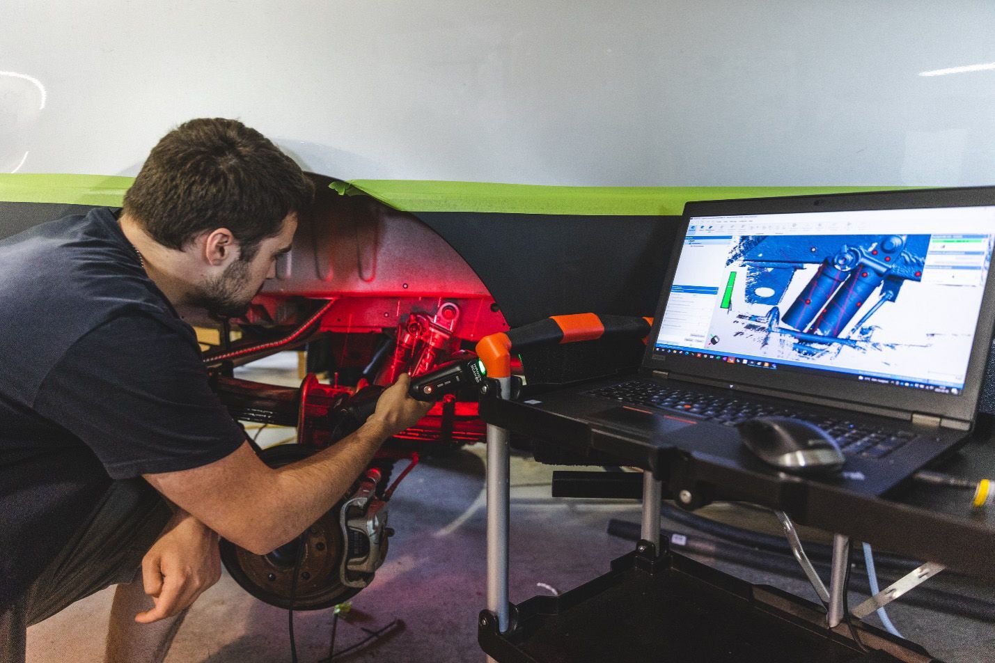 Un homme utilise un outil pour examiner le dessous d'une voiture, un ordinateur portable affichant un schéma à proximité.