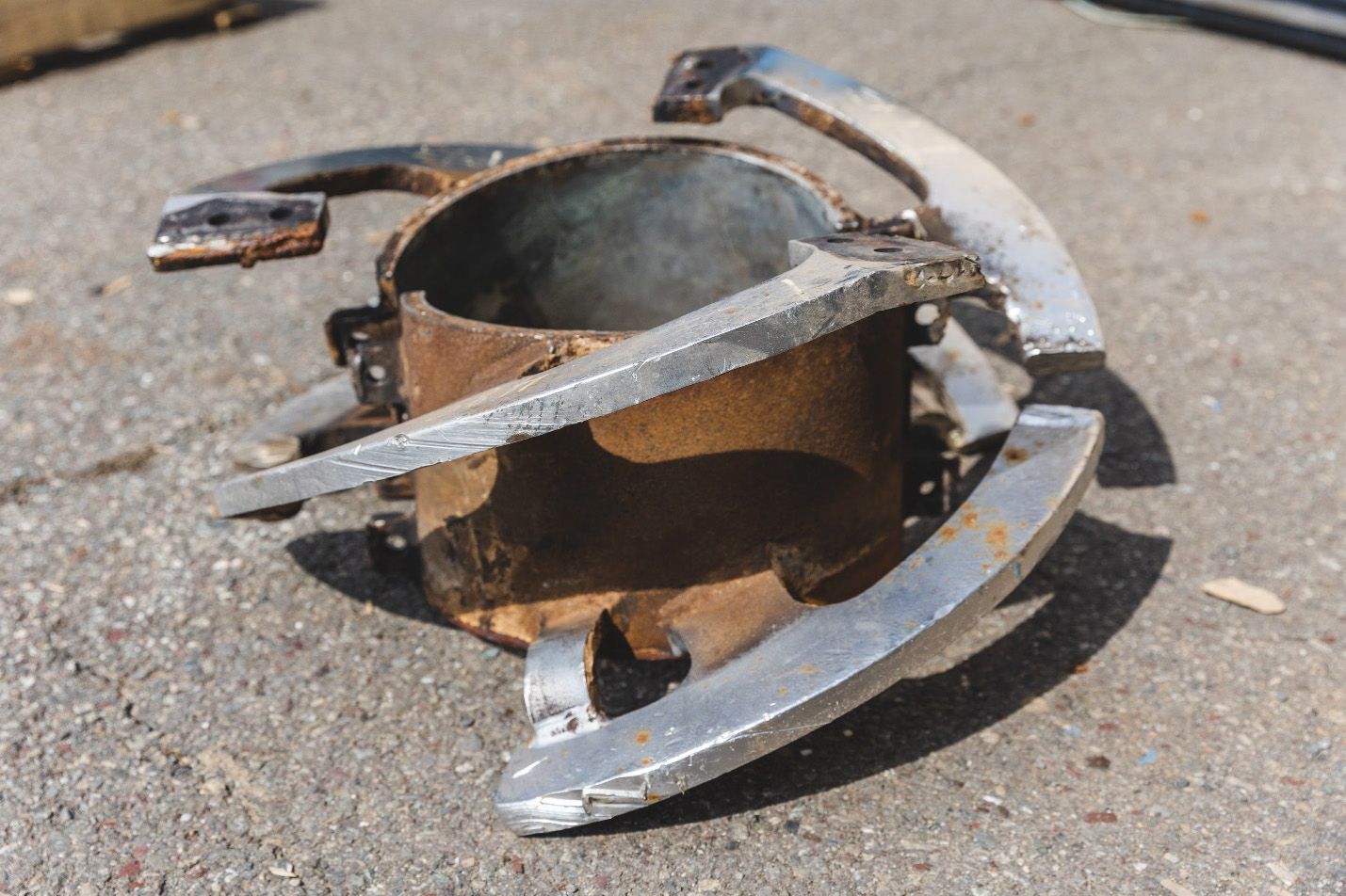 Dispositif métallique rouillé à trois poignées argentées, posé sur une surface en béton.