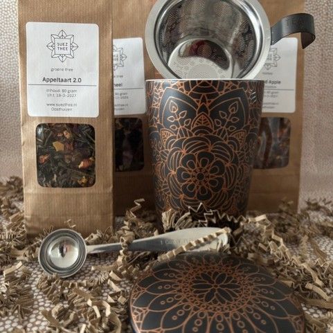 Roze theekopje met deksel, theezakjes en lepel op versnipperd papier; theegeschenkset.