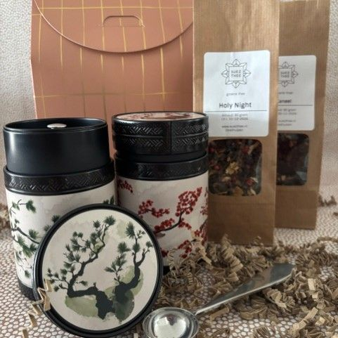 Theecadeauset: mokken, theezakjes, bus, schepje en papieren doosje met decoratief patroon in bruin en goud.