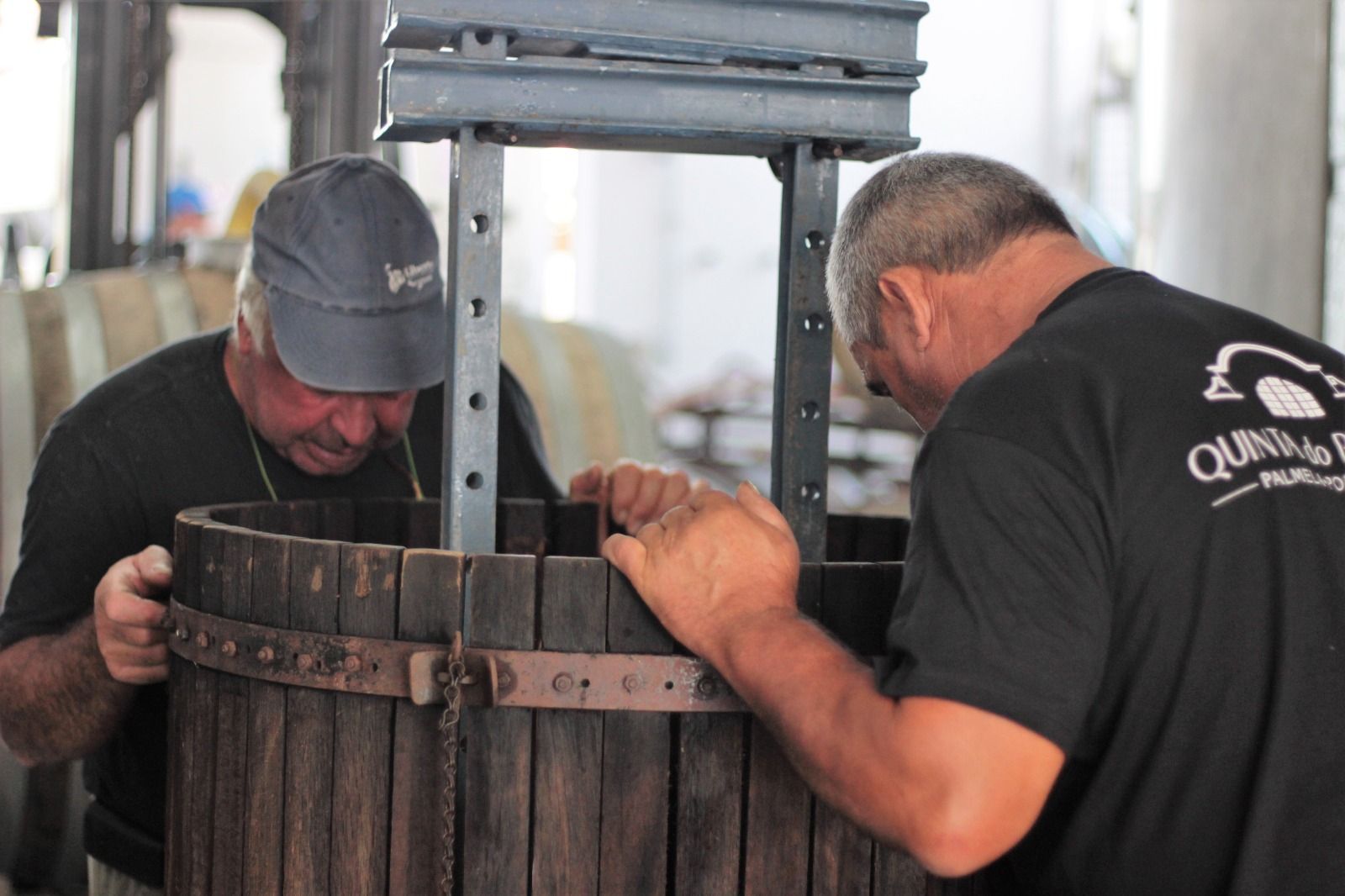 Twee mannen werken met een houten vat onder een metaalpers.