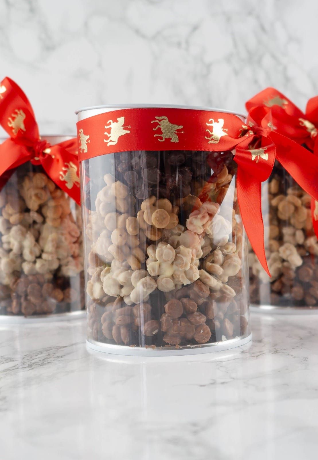 Drie doorzichtige potten gevuld met veelkleurige lekkernijen, vastgebonden met rood lint op marmer.