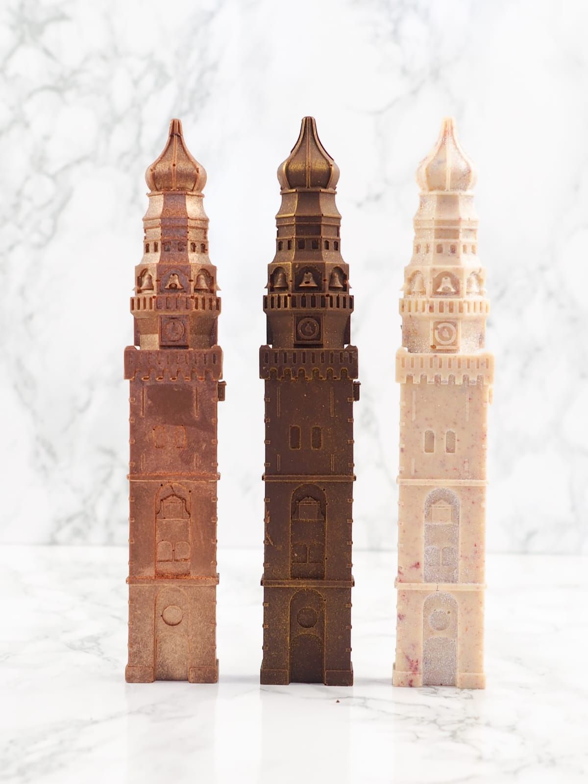 Drie chocoladetorensculpturen in verschillende tinten bruin, staand op een wit oppervlak.