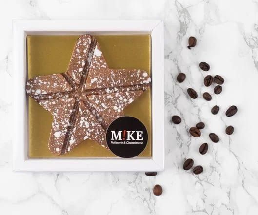 Vier stervormige, gekleurde snoepjes op een wit marmeren oppervlak: rood, oranje, bruin en chocolade.