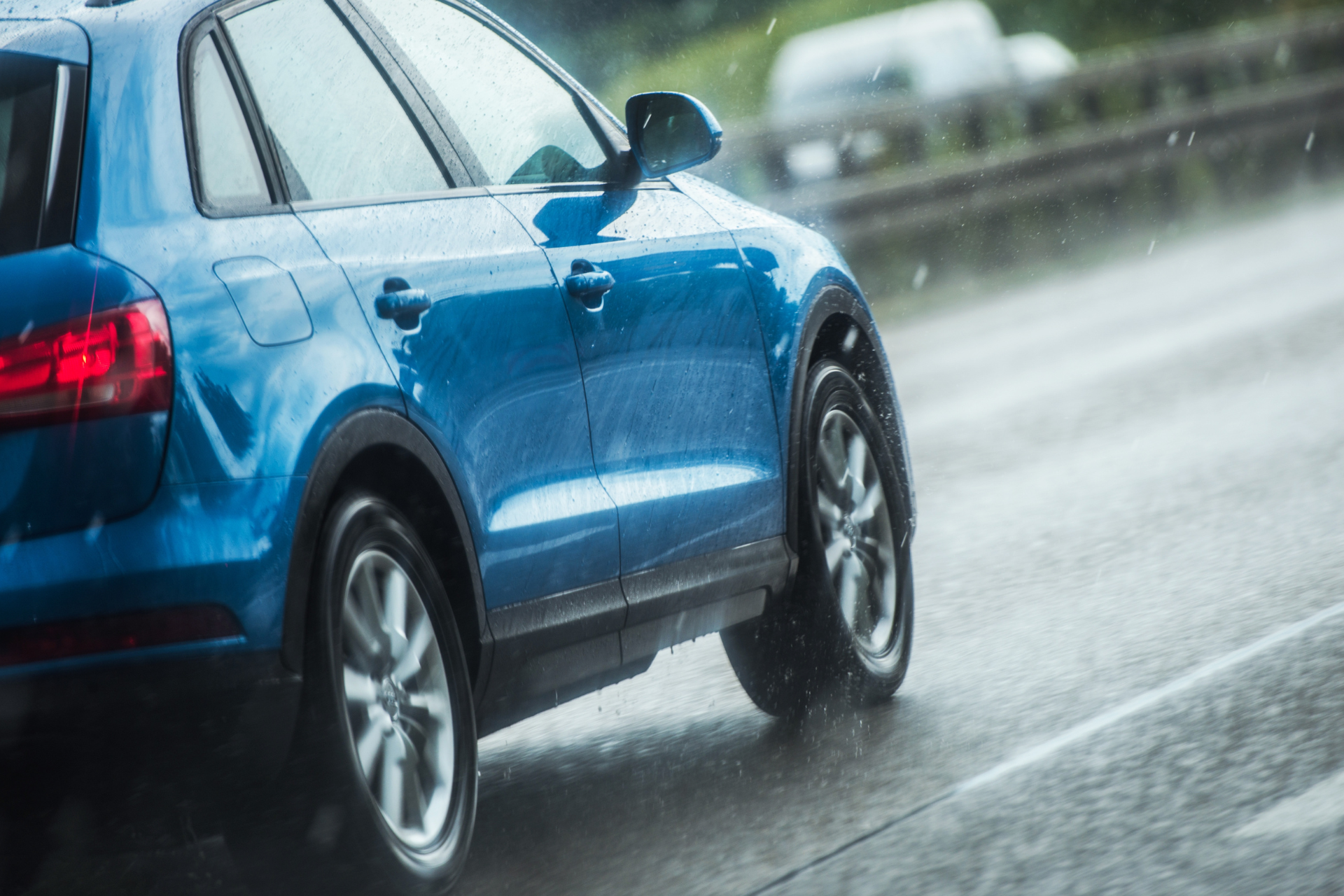 A blue car is driving down a wet road in the rain.