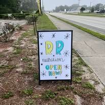 Sidewalk sign by a road reads “RD” with “OPEN NOW!” in colorful letters.